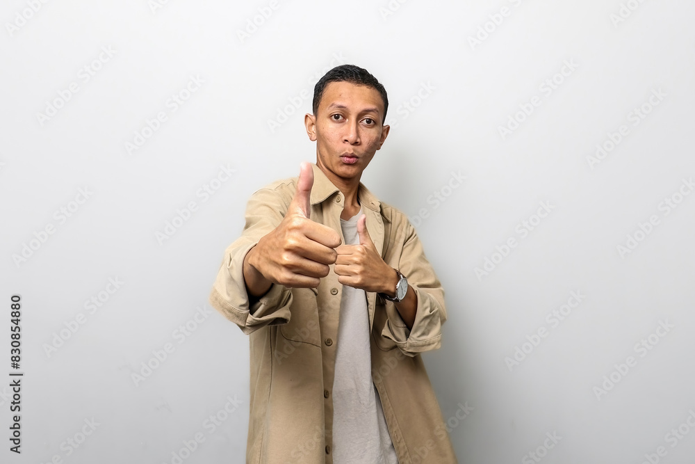Asian man in tan jacket with like or thumb up hand gesture showing his best Asian man in tan jacket with like or thumb up hand gesture showing his best