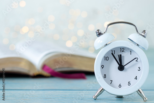 Fotografia Alarm clock and open holy bible book with white bokeh light background