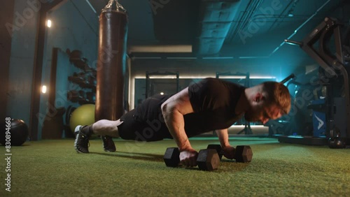 A man in a modern gym focuses on fitness, performing pushups on dumbbells. The gyms artificial turf and exercise equipment create a highenergy environment for his workout routine photo