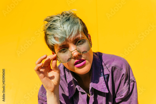 Woman with dyed hair holding sunglasses in front of yellow wall