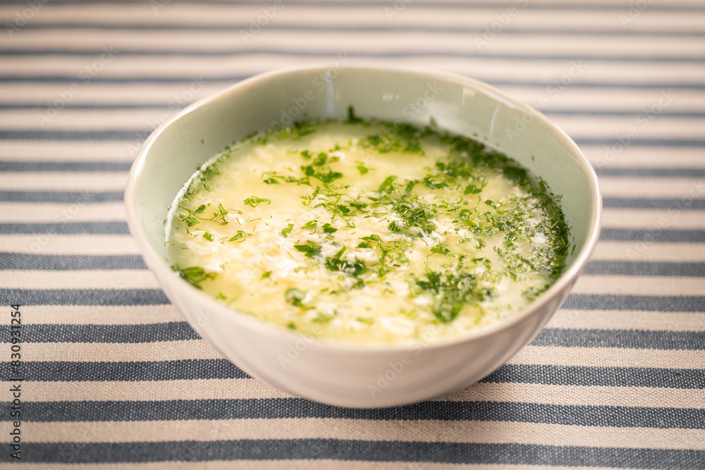 Italian stracciatella egg drop soup with parmesan cheese in white bowl on table. Italian stracciatella egg drop soup with parmesan cheese in white bowl on table.