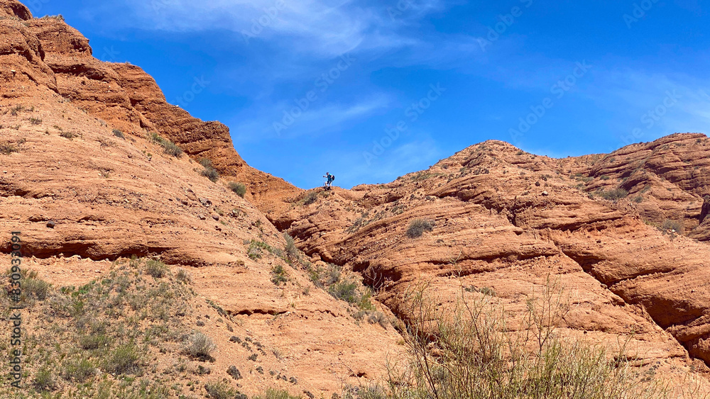 A climber walks along the ridge of the Konorchek canyons in Kyrgyzstan. A man stands on a rocky hillside admiring the scenery. The sky is clear and blue A climber walks along the ridge of the Konorchek canyons in Kyrgyzstan. A man stands on a rocky hillside admiring the scenery. The sky is clear and blue