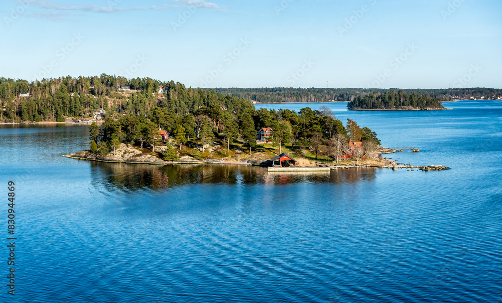 Small island connected with a bridge in Stockholm archipelago in Baltic sea with traditional white and red house at sunny spring evening scenery.