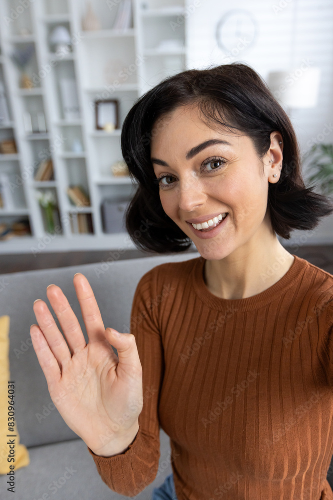 Vertical close-up photo of a young beautiful woman at home, talking on a video call on the phone, greeting and waving Vertical close-up photo of a young beautiful woman at home, talking on a video call on the phone, greeting and waving