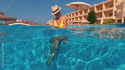 Girl in a hat sitting in the pool enjoys cool on a sunny day. Underwater split