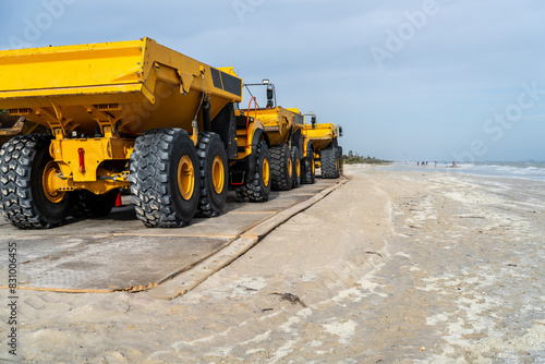 A row of mining type dump trucks on a beach parked on composite construction mats laid on the sand, Sanibel Island, Florida
