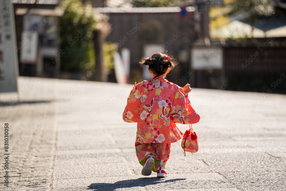 Naklejka premium A little girl in a kimono is running down a street.