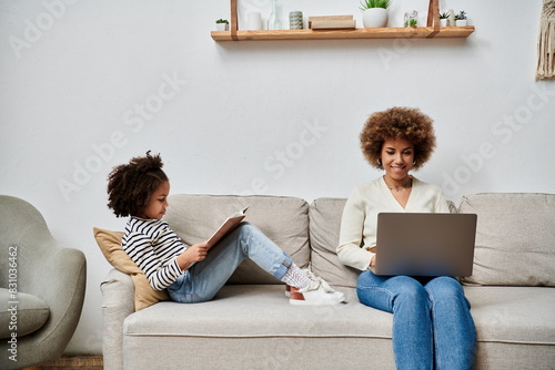 Fotografija An African American mother and daughter happily seated on a couch, engrossed in using a laptop together