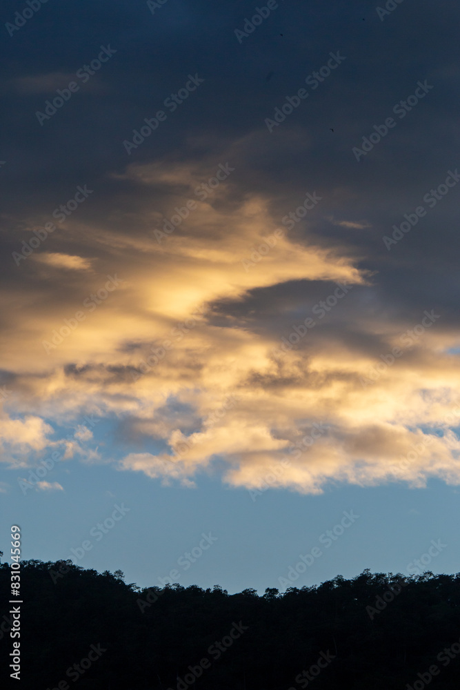 Landscape of thick clouds, orange light hitting the blue sky, silhouettes of trees, forests, and mountains. Area for text in the middle of the image Landscape of thick clouds, orange light hitting the blue sky, silhouettes of trees, forests, and mountains. Area for text in the middle of the image