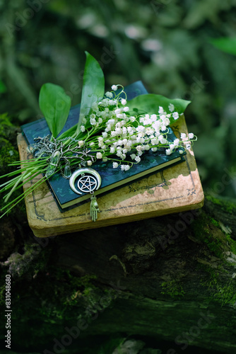 bouquet of Lily of the valley flowers and pentacle amulet with books in forest, natural dark background. symbol of spring season. witchcraft, green magic, spiritual ritual