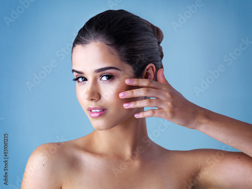Studio, portrait and woman with touch, skincare and cosmetics for natural makeup with healthy skin glow. Beauty, dermatology and face of girl with confidence, wellness and care on blue background.