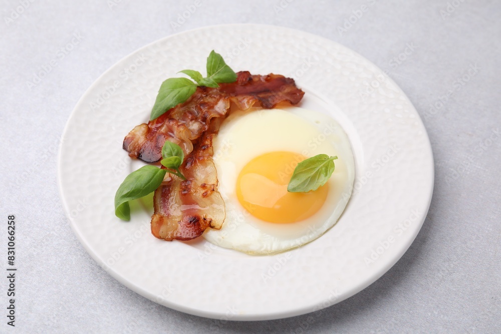 Fried egg, bacon and basil on light grey table Fried egg, bacon and basil on light grey table
