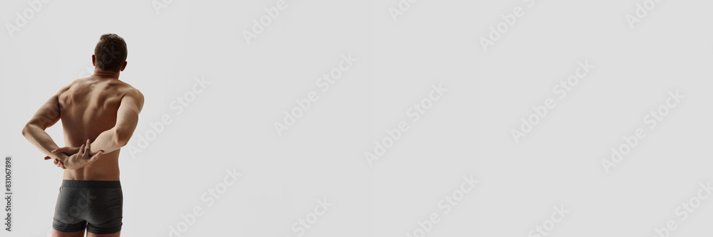 Obraz premium Back view image of man with muscular, sportive relief body shape standing in underwear, boxers isolated on grey studio background. Concept of male beauty, body care, fitness, sport, health. Banner