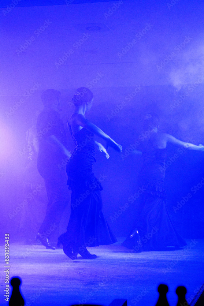 Silhouettes of a group of Spanish flamenco dancers on the stage of the theatre on a dark blue background. Space for your design.