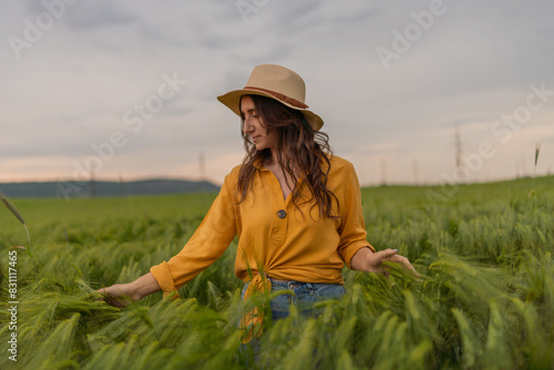 A woman in a yellow shirt and straw hat stands in a field of tall grass