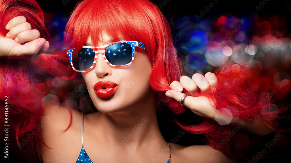 Fototapeta premium Red-haired woman celebrates 4th of July wearing American flag sunglasses and pouting her sensual lips at camera