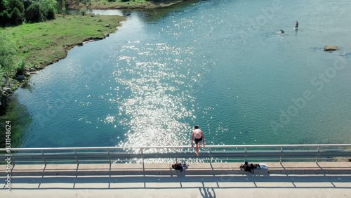 Slow motion drone shot of young man jump into water from bridge into river. Summer camp or holidays in countryside. Hot weather activity, swimming in cold water of mountain river photo