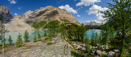 View along a rock ridge at a large rocky mountain and two blue lakes. The blue sky has scattered clouds.
