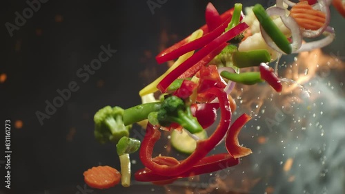 Closeup of chef preparing and throwing vegetable mix on frying pan on fire. Preparation fresh appetizing food. Vegetables flying into the pan in slow motion. Healthy vegetarian food cooking close-up
