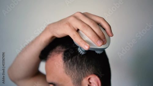  man massages his head with an electric massager for hair growth