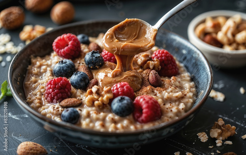 Oatmeal bowl with a spoon of creamy peanut butter, fresh raspberries, blueberries, and nuts on a rustic table