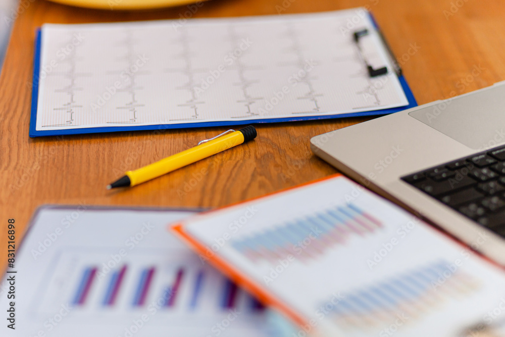 A yellow pen sits on a desk next to a stack of papers. The papers are filled with graphs and numbers, and the pen is placed on top of one of them A yellow pen sits on a desk next to a stack of papers. The papers are filled with graphs and numbers, and the pen is placed on top of one of them