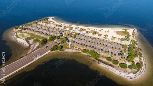 Aerial view of Fred Howard Park in Tarpon Springs, Florida, featuring parking lots, palm trees, sandy beaches, and surrounding blue waters under a clear sky.