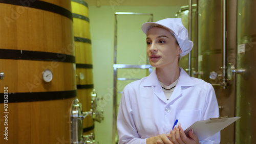 Winemaker woman checking and examining producing wine at winery in factory, inspector checking quality and fermenting wine storage in tank or barrel at room, industrial and manufacture concept.