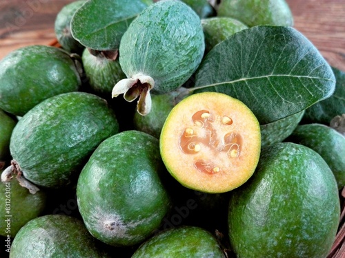 Green feijoa fruit slice & feijoa leaf (Acca sellowiana) in bowl on wooden background. Tropical feijoa or pineapple guava fruit exotic green fruit. Raw acca sellowiana plant, guavasteen green fruit