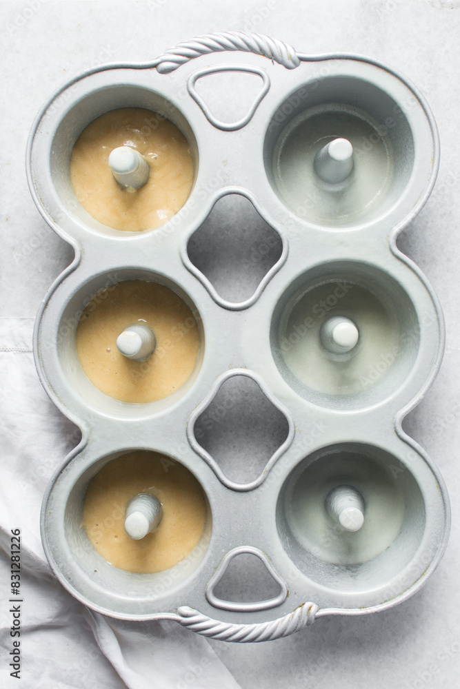 Overhead view of vanilla cake batter in mini bundt cake pan, top view of cake batter in silver bundtlette baking pans, process of making mini bundt cakes Overhead view of vanilla cake batter in mini bundt cake pan, top view of cake batter in silver bundtlette baking pans, process of making mini bundt cakes