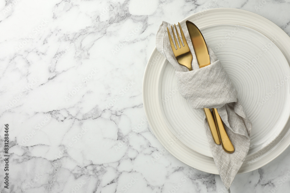 Stylish setting with cutlery, napkin and plates on white marble table, top view. Space for text Stylish setting with cutlery, napkin and plates on white marble table, top view. Space for text