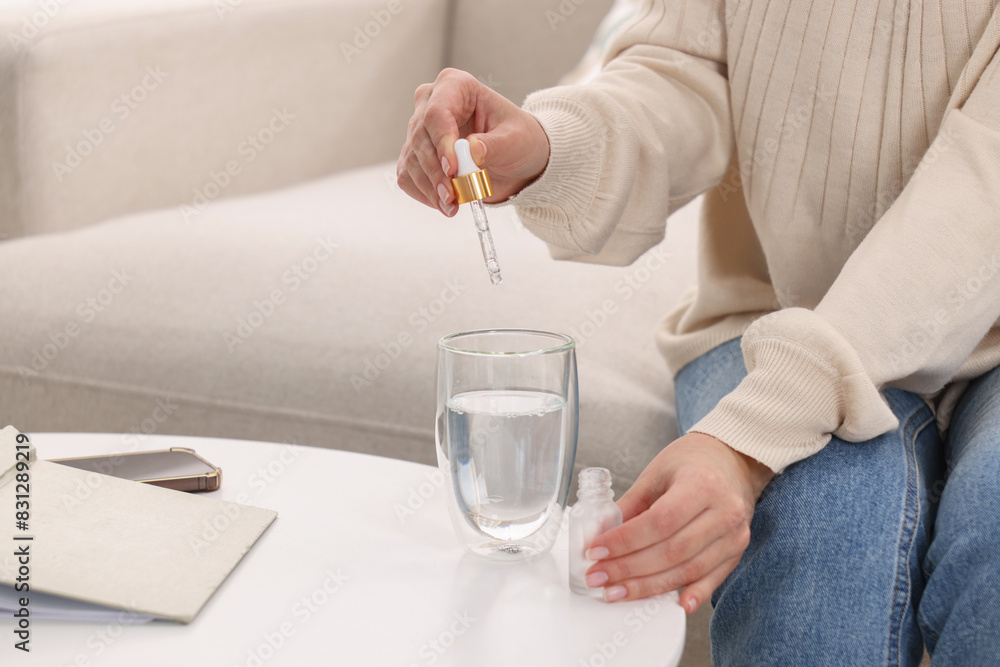Obraz premium Woman dripping food supplement into glass of water on white table indoors, closeup