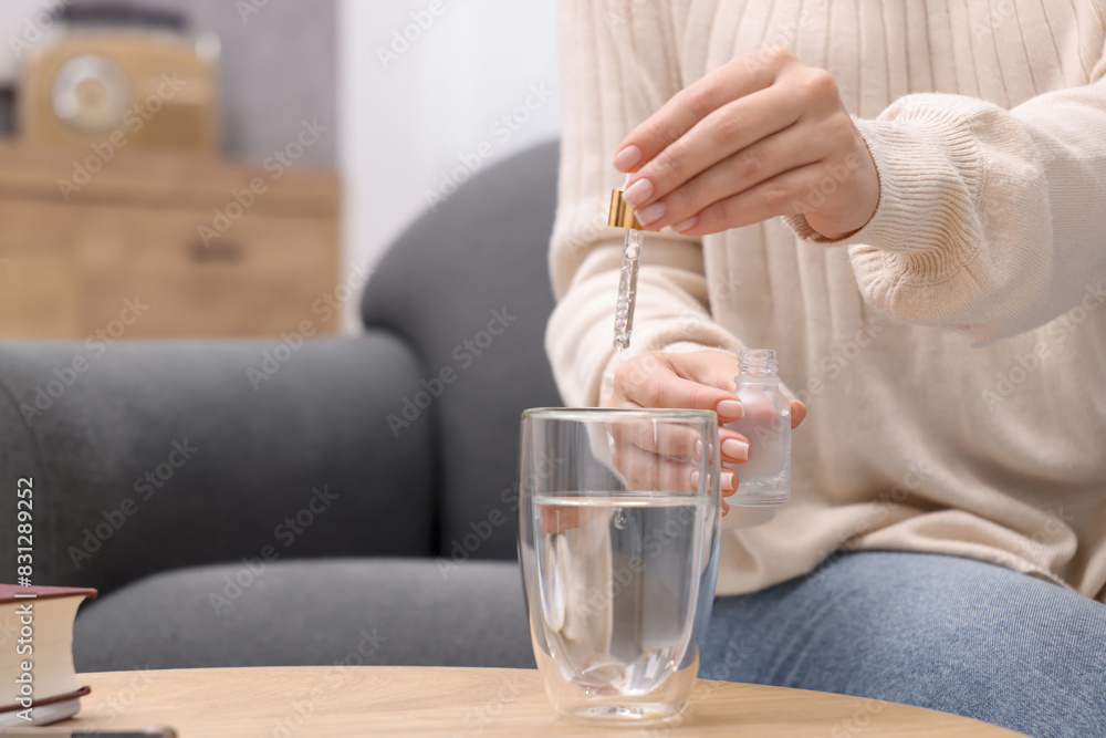 Woman dripping food supplement into glass of water on wooden table indoors, closeup. Space for text Woman dripping food supplement into glass of water on wooden table indoors, closeup. Space for text