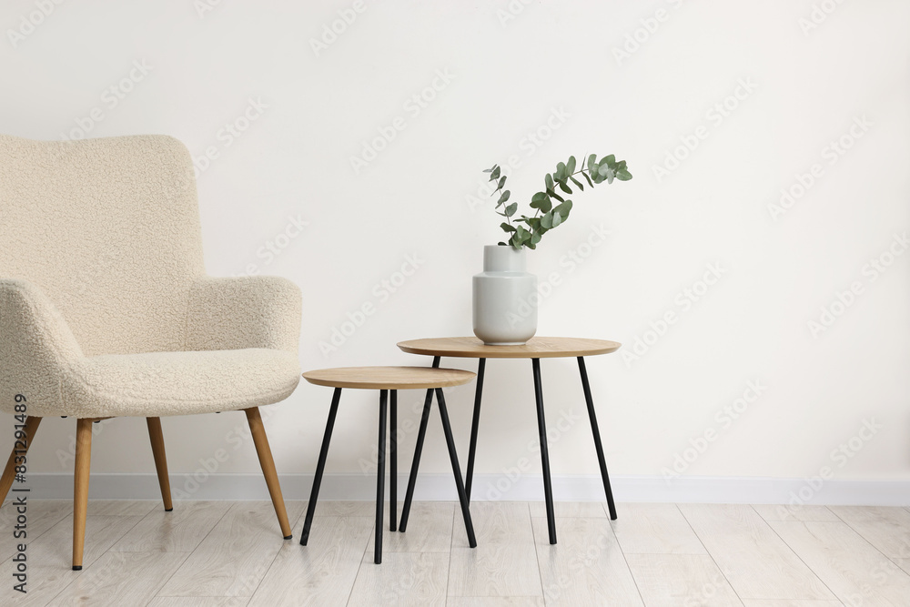 Comfortable armchair, nesting tables and eucalyptus indoors, space for text Comfortable armchair, nesting tables and eucalyptus indoors, space for text