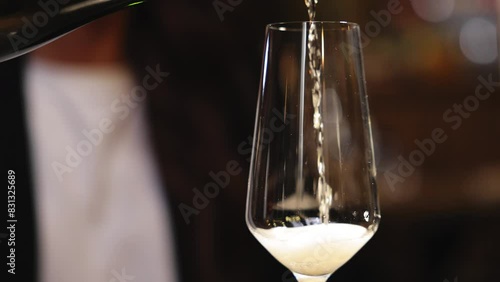 Unrecognizable waiter pouring sparkling wine from dark bottle and creating splashing foam with bubbles in flute glass. Attentive server refilling drinks of visitors of expensive restaurant.