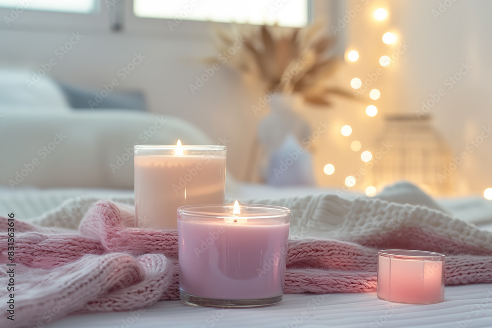 Three lit candles and knitted blankets on bed, soft and cozy bedroom setting with bokeh lights Three lit candles and knitted blankets on bed, soft and cozy bedroom setting with bokeh lights