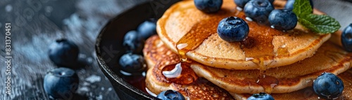 A cast iron skillet filled with golden brown pancakes drizzled with warm maple syrup and scattered with fresh blueberries. photo