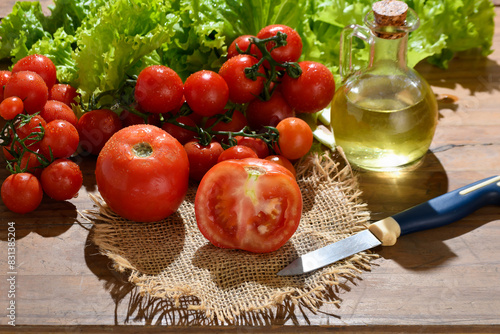  tomato, sliced tomato, cherry tomato, lettuce and olive oil are placed on a wooden base.
