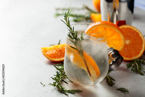 Refreshing drink with natural ice, orange, and rosemary in a frozen glass.
