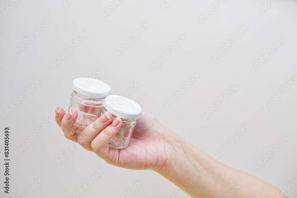 Woman's hand holding little glass bottles for honey or liquid. On a white wall background. Transparent glass medical bottles . Isolated studio photo. Woman's hand holding little glass bottles for honey or liquid. On a white wall background. Transparent glass medical bottles . Isolated studio photo.