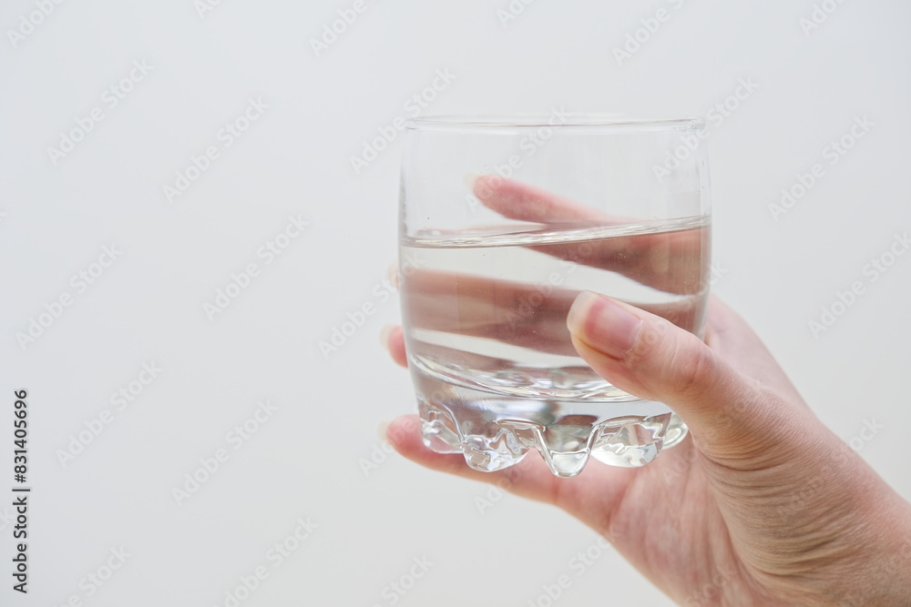 Woman's hand holding glass full of water on a white wall background. Transparent glass in the frame. Isolated studio photo. Digestive care and refreshment concept Woman's hand holding glass full of water on a white wall background. Transparent glass in the frame. Isolated studio photo. Digestive care and refreshment concept