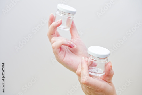 Woman's hands holding little glass bottles for honey or liquid. On a white wall background. Transparent glass medical bottles . Isolated studio photo. 