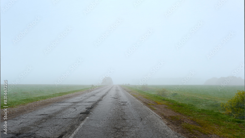 Fototapeta premium Broken asphalt road on an early foggy morning. Road in need of repair.