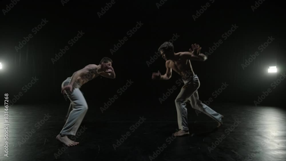 Group of a professional dancers are practicing capoeira in darkness against a spotlight on a black background of studio. Afro-Brazilian martial art that combine elements of dance. Group of a professional dancers are practicing capoeira in darkness against a spotlight on a black background of studio. Afro-Brazilian martial art that combine elements of dance.