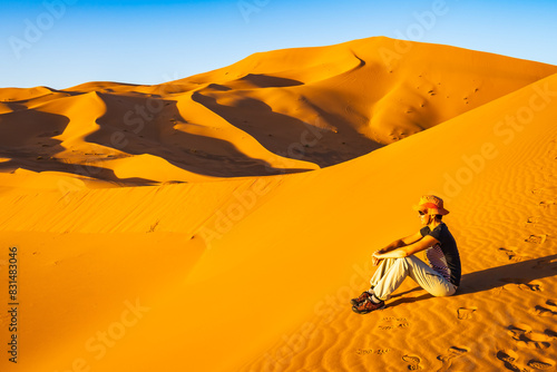 Young woman tourist with hat sitting on sand dune at Erg Chebbi Sahara desert at sunset near Merzouga town  Morocco  North Africa