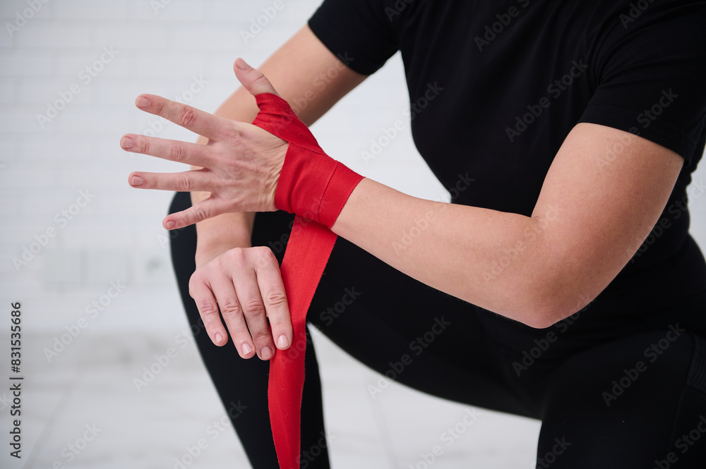 Fototapeta premium Selective focus on hands of female fighter preparing for boxing competition challenge training, tying tapes before putting boxing gloves, isolated over white background. Sport and martial art concept