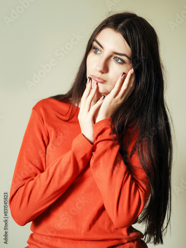 Portrait of a young teenager girl in red shirt on light color background. Model with long rich hair. Hands frame her face. Calm face expression. Beauty image.