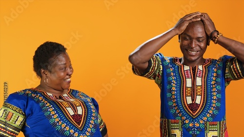 Joyful african american people laughing at something in studio, having fun with jokes and being amused over orange background. Married couple enjoying laugh on camera, silly partners.