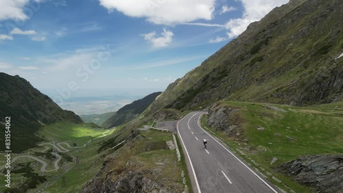 Aerial view of cyclist riding in Carpathian mountains on winding road.  Transfagarasan, Romania. Fit female cyclist is riding bicycle between mountain hills. Pedaling through nature. Transylvania