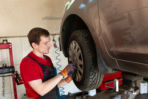 a mechanic stands by a car in a car service center. master removes a wheel from a car, repair, wheel replacement © Svetlana